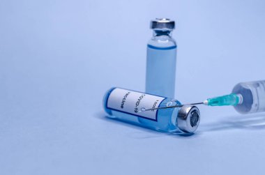 Mavi arka planda şırıngayla cam şişelerde Coronavirus aşısı.