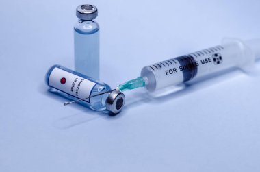 Mavi arka planda şırıngayla cam şişelerde Coronavirus aşısı.