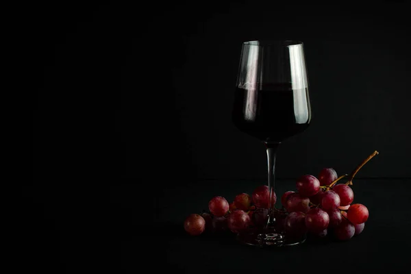glass with red wine on a dark background and a bunch of red grapes