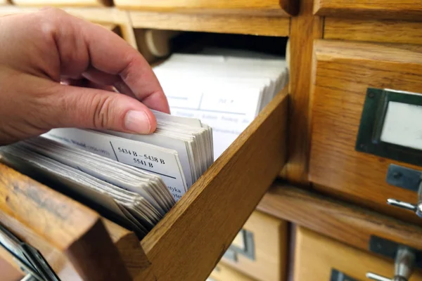 female hand searching through archive cards in an old wooden fil