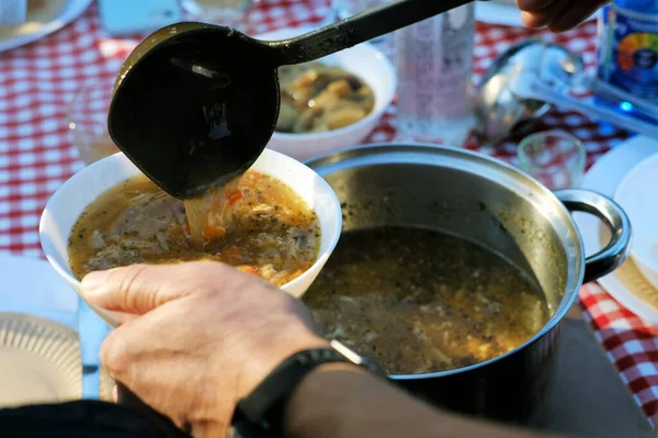 Lezzetli, geleneksel ciladan yapılmış çorba tabaklarını bahçe partisinde bir kaseye dolduran adam.