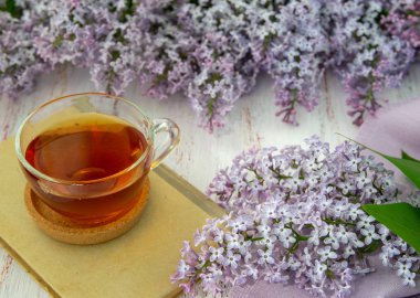 Leylak ve yapraklarıbahar çiçekleri, çay bir fincan ve ahşap bir arka plan üzerinde bir kitap. Dekoratif çerçeve, üst görünüm.