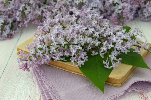 Spring flowers of lilac and leaves, book on wooden background. Decorative frame, close-up,  top view.