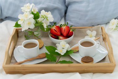 İki kişilik yatakta kahvaltı. Kahve, çilek ve kurabiye ile ahşap tepsi. Narin beyaz çiçekler ile Takı.
