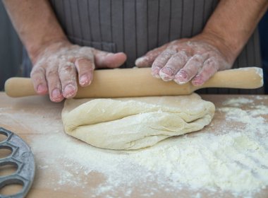 Şefin elleri, hamuru gri bir arka plan üzerinde mantı iğnesi için frezeleme kalıplarının yanında tahta bir masada yoğuruyor. Pişirme işlemi 