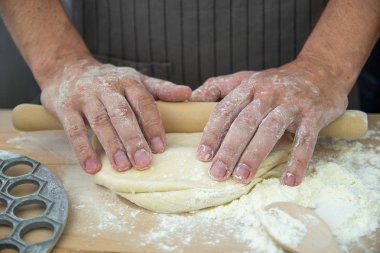 Şefin elleri, hamuru gri bir arka plan üzerinde mantı iğnesi için frezeleme kalıplarının yanında tahta bir masada yoğuruyor. Pişirme işlemi 