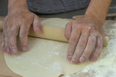 Şefin elleri, hamuru gri bir arka plan üzerinde mantı iğnesi için frezeleme kalıplarının yanında tahta bir masada yoğuruyor. Pişirme işlemi 