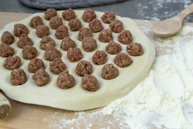 Hamur ahşap bir masada mantı veya köfte pişirmek için kıyma şeklinde bir oklava ile dışarı haddelenir, pişirme işlemi üst görünümü.
