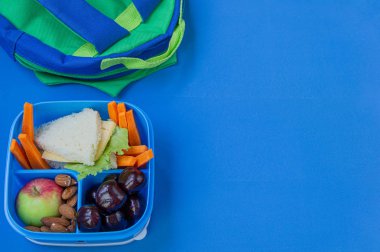 Okul malzemeleri ile mavi arka plan üzerinde sandviç, fındık, sebze ve meyve ile Okul öğle yemeği kutusu. Kopyalama alanı.