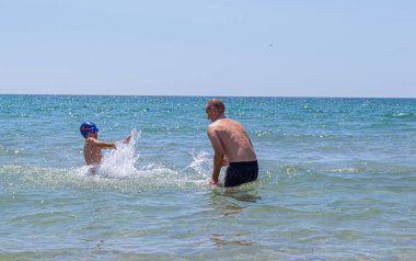 Baba ve oğul denizde suda oynarlar. Su sıçratıp neşeyle gülüyorlar. Deniz suyu spreyi.