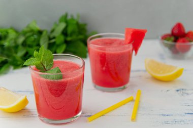 Bardakna nane, limon ve çilek ile soğuk karpuz smoothie . Ahşap açık mavi arka plan üzerinde, yaz için renkli serinletici içecekler.