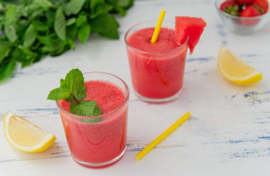 Bardakna nane, limon ve çilek ile soğuk karpuz smoothie . Ahşap açık mavi arka plan üzerinde, yaz için renkli serinletici içecekler.