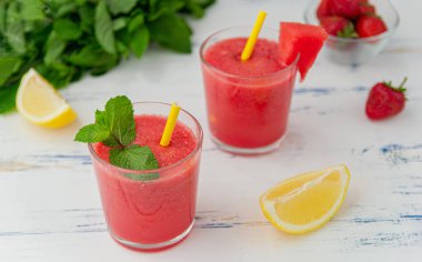 Bardakna nane, limon ve çilek ile soğuk karpuz smoothie . Ahşap açık mavi arka plan üzerinde, yaz için renkli serinletici içecekler.
