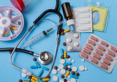 Sağlık ve tıp kavramı. Çeşitli ilaç tabletleri, stetoskop ve hap kutuları mavi arka plan üzerinde. Dağıtım ve hap alarak hatırlatma