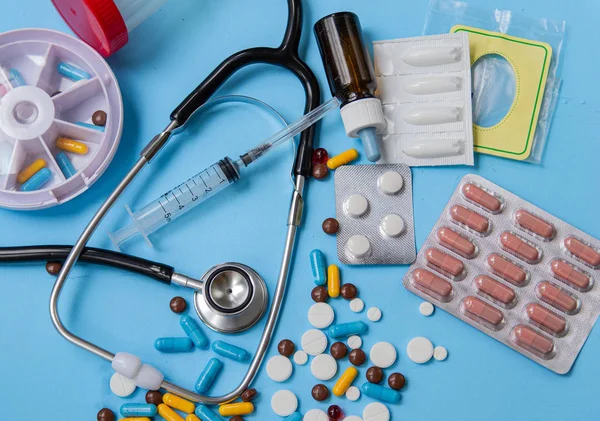 Sağlık ve tıp kavramı. Çeşitli ilaç tabletleri, stetoskop ve hap kutuları mavi arka plan üzerinde. Dağıtım ve hap alarak hatırlatma