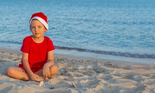 一个戴着红色圣诞帽的孩子在海里玩耍 圣诞老人海上圣诞假期的概念 复制空间 — 图库照片