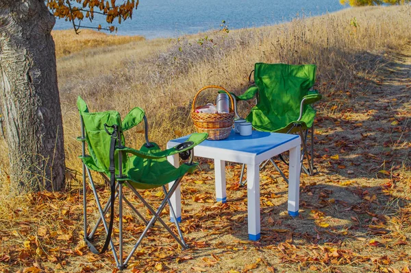 Autumn picnic in the mountains on the lake, a warm autumn day. Basket with food on the table. Herbal tea, thermos on the background of autumn forest and mountains.Autumn concept.