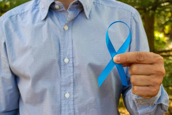 Awareness of prostate cancer, a man holding a light blue ribbon on a background of autumn leaves. To support people living with and patients . Men\'s health and the concept of world cancer day.