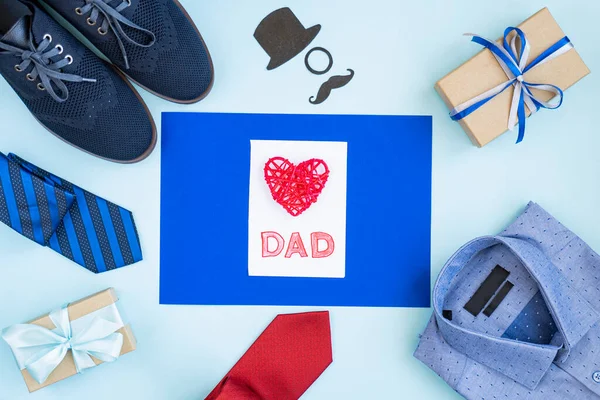 Background of father\'s Day. A gift box, shoes, tie, shirt, and holiday decoration on a light blue table. Top view, flat lay, copy space