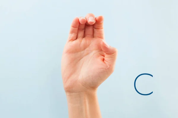 American sign language. Female hand showing letter C isolated on blue background.