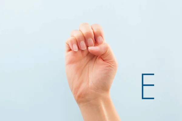American sign language. Female hand showing letter E isolated on blue background.