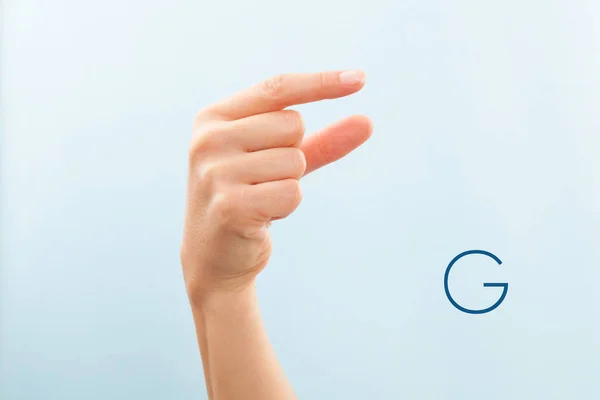 American sign language. Female hand showing letter G isolated on blue background.