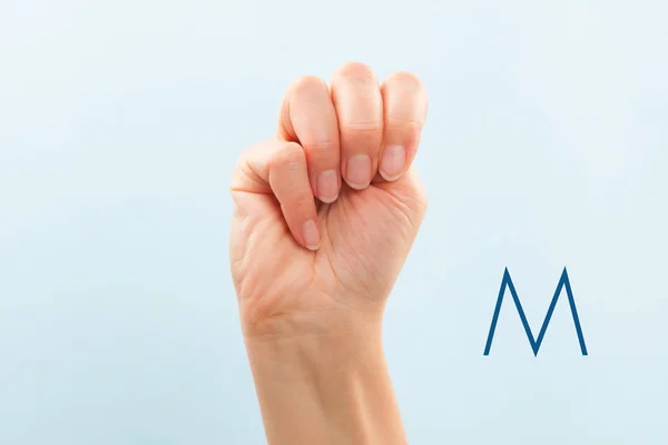 American sign language. Female hand showing letter M isolated on blue background.