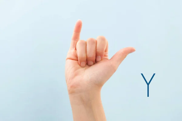 American sign language. Female hand showing letter Y isolated on blue background.