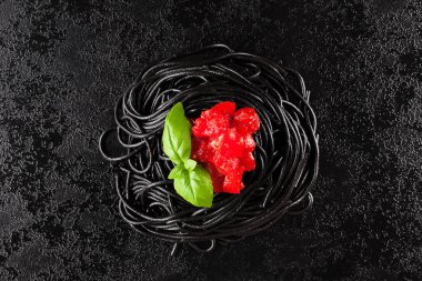 Kırmızı domates sosu ve siyah tablo taze fesleğen ile siyah spagetti.