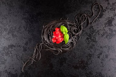 Siyah mürekkep balığı spagetti fesleğen ve karanlık yüzeyi yukarıdan domates ile.