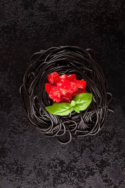 Siyah mürekkep balığı spagetti taze fesleğen ve yukarıdan domates karanlık yüzeyi ile mürekkep. Mutfak gıda.
