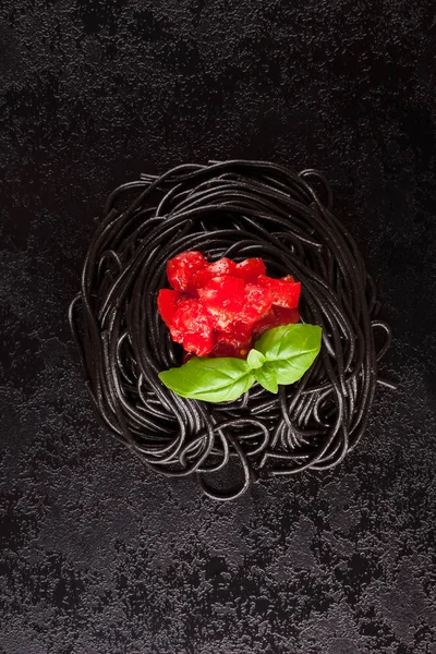 Siyah mürekkep balığı spagetti taze fesleğen ve yukarıdan domates karanlık yüzeyi ile mürekkep. Mutfak gıda.