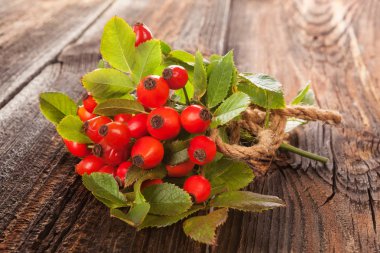 Ahşap zemin üzerine yeşil yaprakları ile kırmızı rose hips demet. Dokunulmazlık ve vitamini bitki.