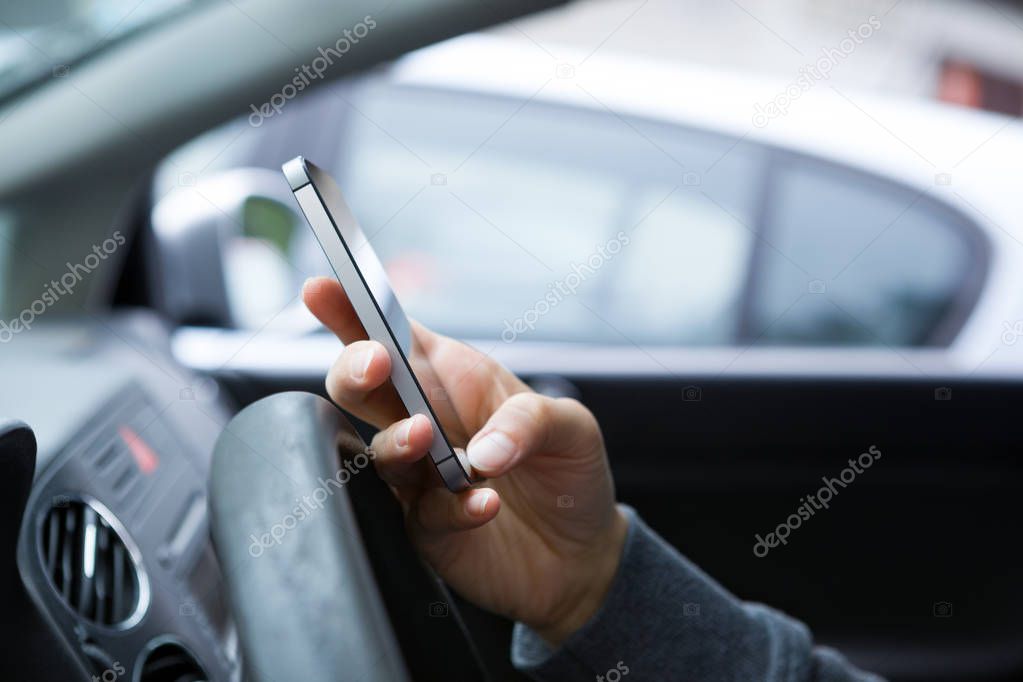 Hand using phone sending a text while driving to work.