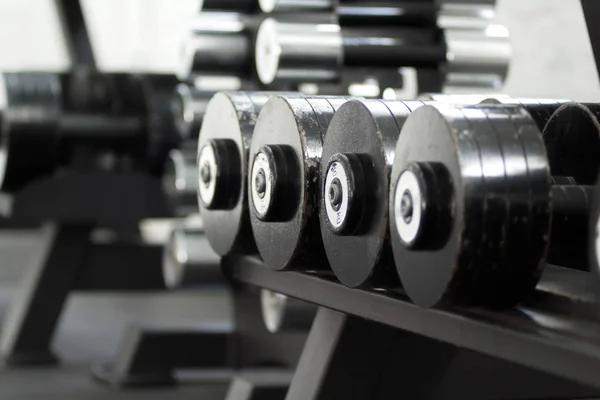 Rows of metal dumbbells on rack in the gym. Weight training equipment.