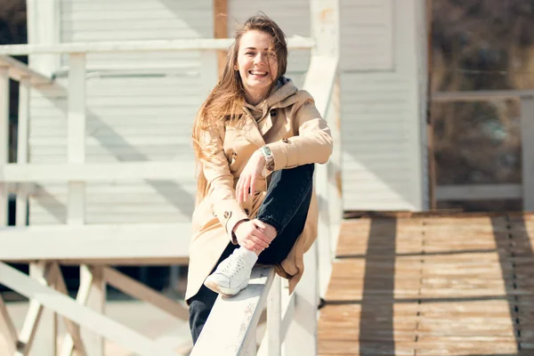 Youth freedom. Happy young woman. Beautiful long-haired, looking and smiling girl sitting on a wooden board on the beach