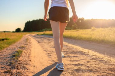Egzersiz, fitness ve sağlıklı yaşam tarzı için çalışan kavram. Atlet koşucu ayakları gün doğumunda tarlanın karşısındaki toprak yolda koşuyor.