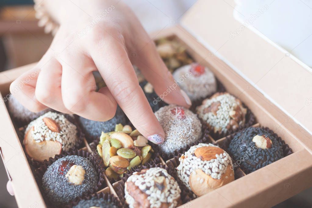 The box with healthy organic sweets with dried fruits, nuts, banana, dates and honey - vegan raw snack. Female hand takes a vegan candy.