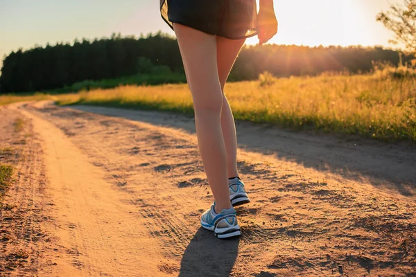 Sport legs. Close up.  Athlete runner feet running on the dirt road across the field in the sunrise.