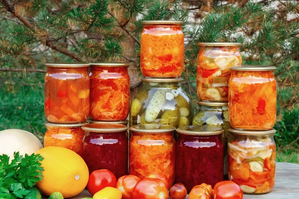 Several homemade jars of canned vegetables and fresh vegetables on a wooden table - image — Stock Photo, Image