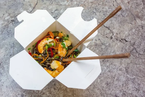 Traditional Chinese takeaway fast food - buckwheat soba noodles with vegetables and shrimps packed in a cardboard box with chopsticks - photo, image