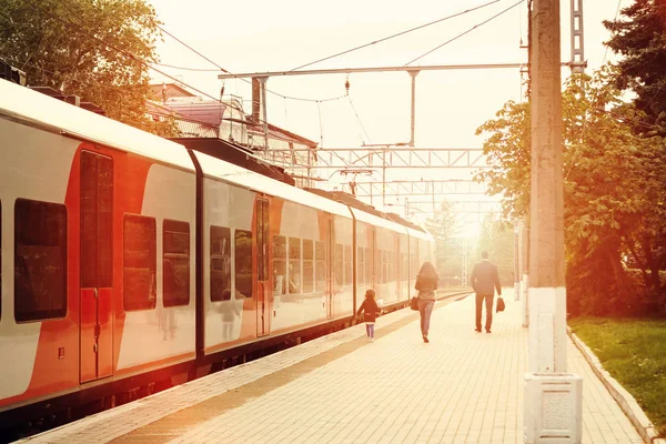 Family of passengers of a train arriving on the platform disappears into the distance in the light of sunset — Stock Photo, Image