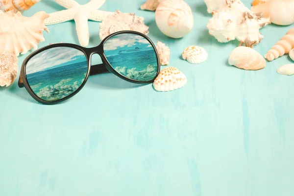 Modré mořské pozadí s slunečními brýlemi a lastury, letní dovolenou a koncept dovolené — Stock fotografie