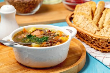 Mavi bir masa üzerinde ahşap bir tahta üzerinde beyaz bir kapta tavuk ile Mercimek çorbası
