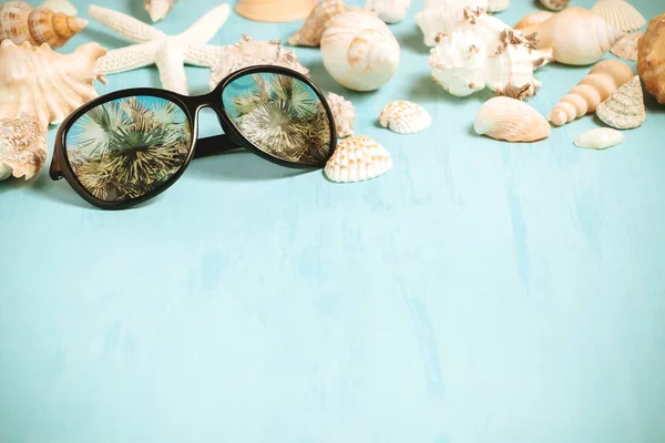 Modré mořské pozadí s slunečními brýlemi a lastury, letní dovolenou a koncept dovolené — Stock fotografie