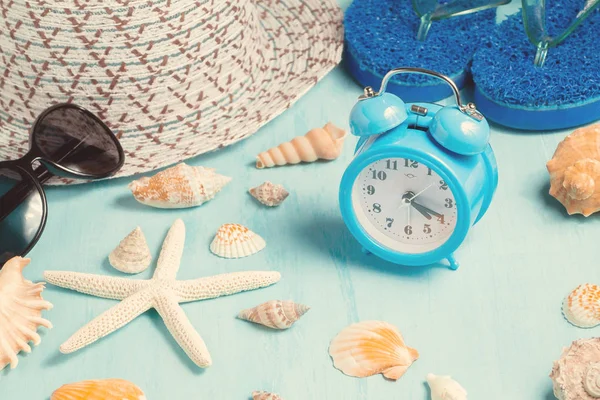 Mušle, budík a plážové příslušenství na modrém stole-letní prázdniny a v době dovolené — Stock fotografie