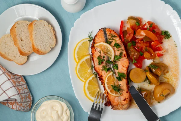 Baked salmon fillet medallion with salad of pickled vegetables and mushrooms on a white plate on a blue background, top view, flatlay — Stock Photo, Image