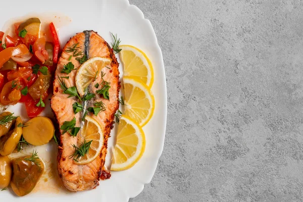 Baked salmon fillet medallion with salad of pickled vegetables and mushrooms on a white plate on a gray background, top view, flatlay, place for text, copy space — Stock Photo, Image