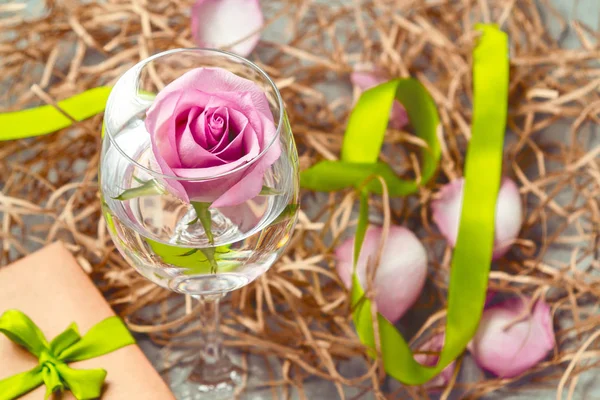 Rosa rosa en un vaso con agua y decoraciones sobre la mesa — Foto de Stock