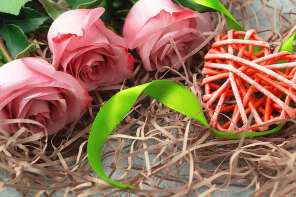 Ramo de rosas rosadas y un corazón de mimbre con decoraciones en la mesa un concepto de amor y felicitaciones por un ser querido — Foto de Stock